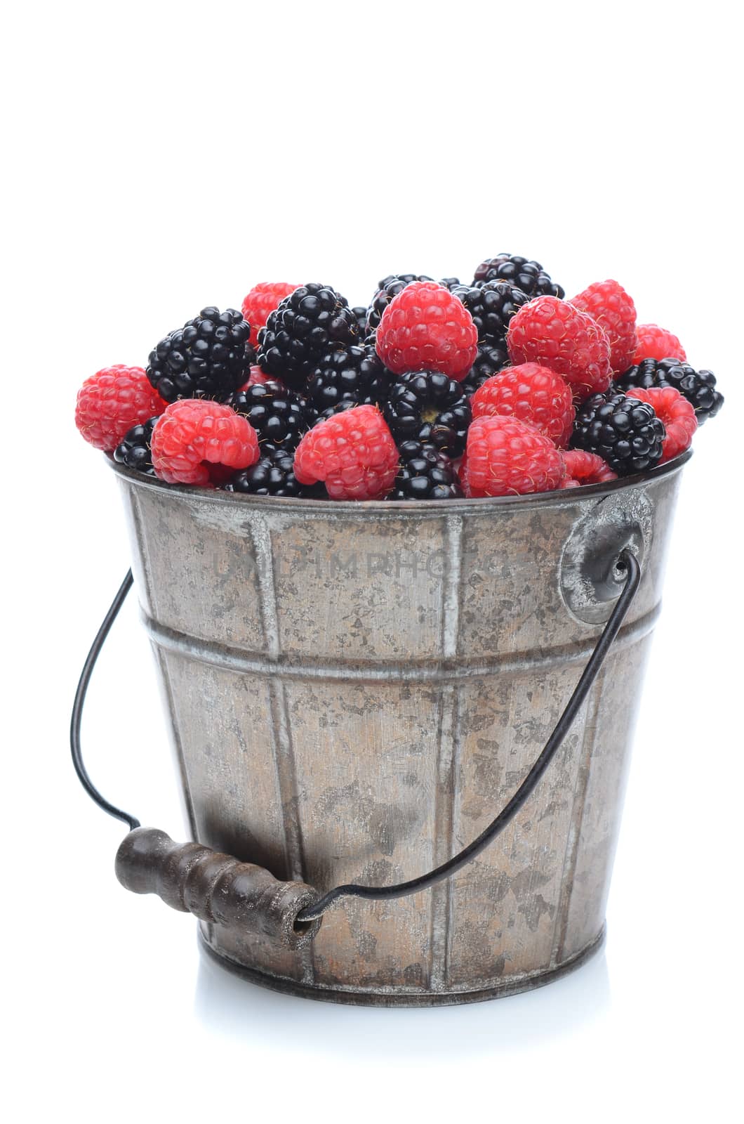 A pail full of freshly picked blackberries and raspberries. Vertical format isolated on a white background with slight reflection.