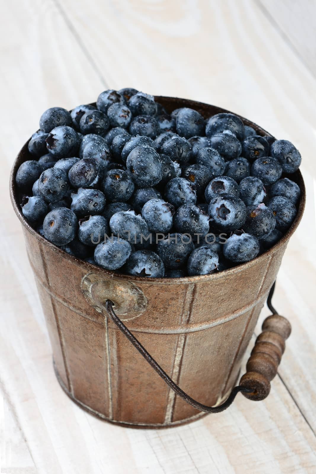 Closeup of a bucket of blueberries on a rustic farmhouse style table. Vertical format shot from a high angle with shallow depth of field. The fresh picked berries are covered with a mist.