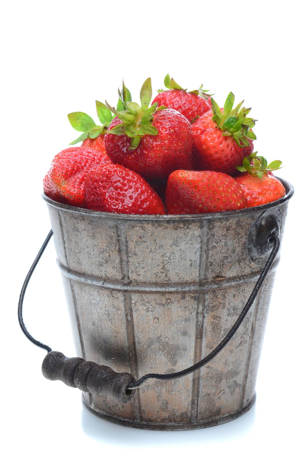 A pail full of freshly picked strawberries. Vertical format isolated on a white background with slight reflection.