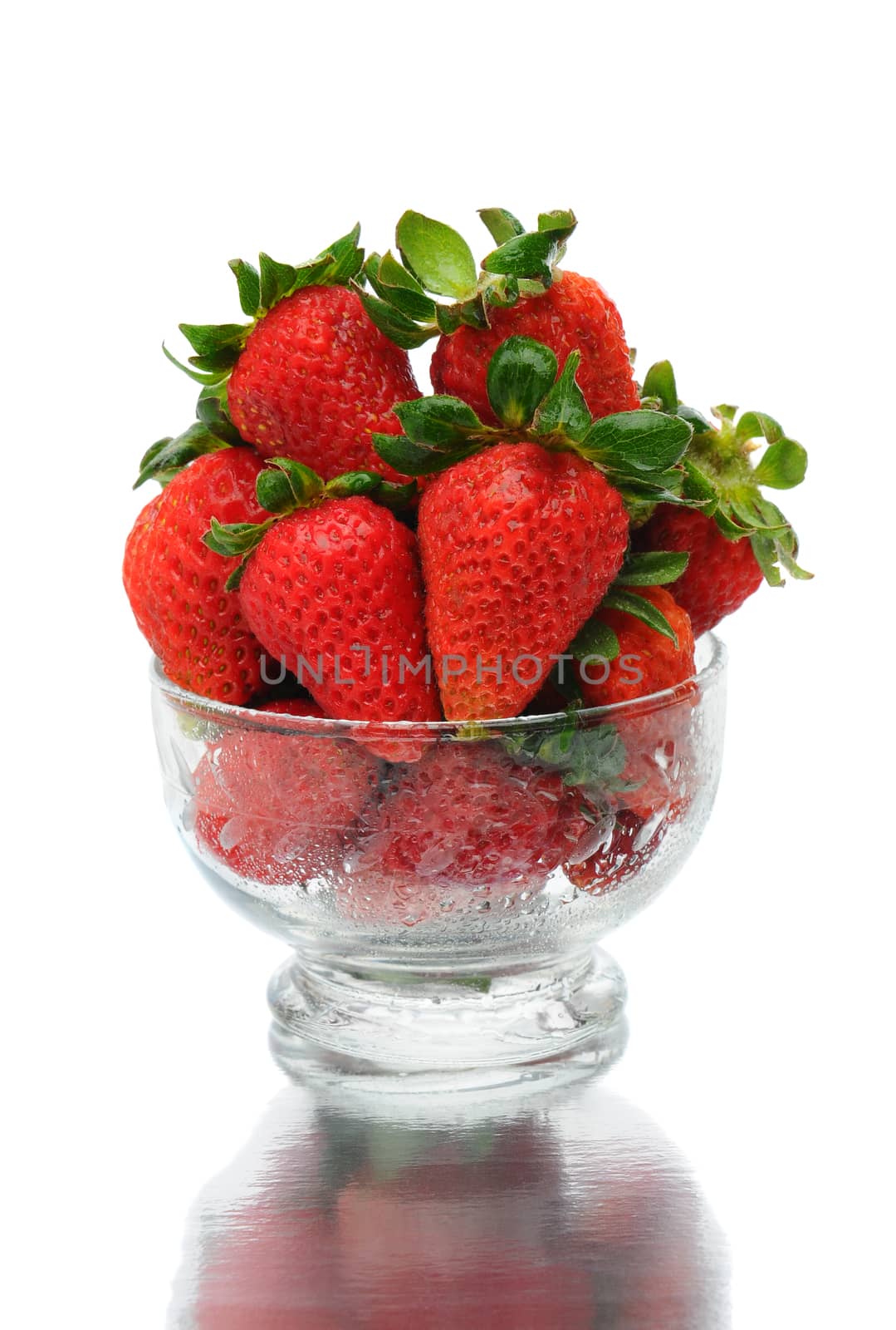 Closeup of fresh picked strawberries in a glass bowl with reflection over a white background.