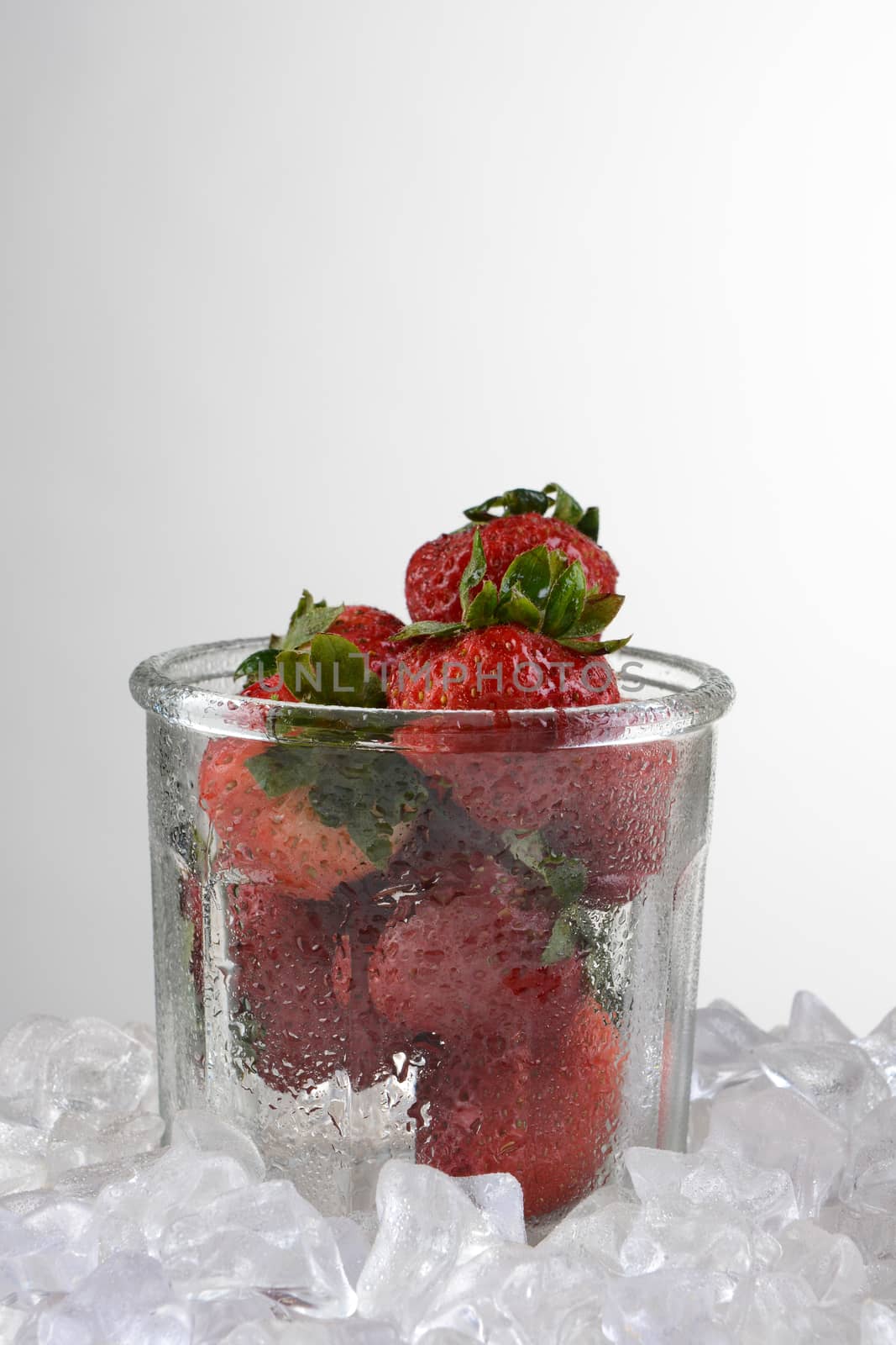 An old fashioned jar with fresh picked strawberries surrounded by crushed ice. Vertical format on a light to dark background with copy space.