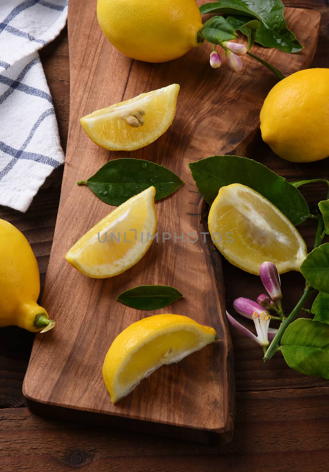 Still life of a group of lemons, whole and cut, on a cutting board. Leaves and lemon flowers and kitchen towel in vertical format.