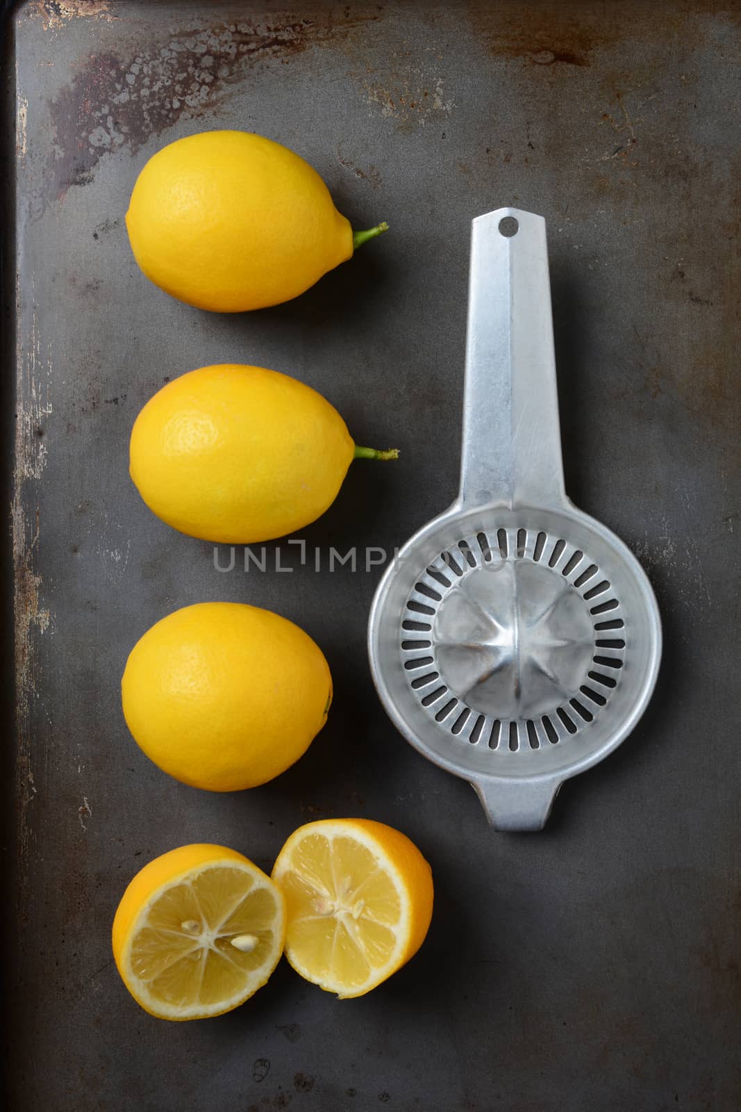 High angle shot of a group of lemons, three whole and one cut, on a metal baking sheet with an old fashioned juicer. Horizontal format.