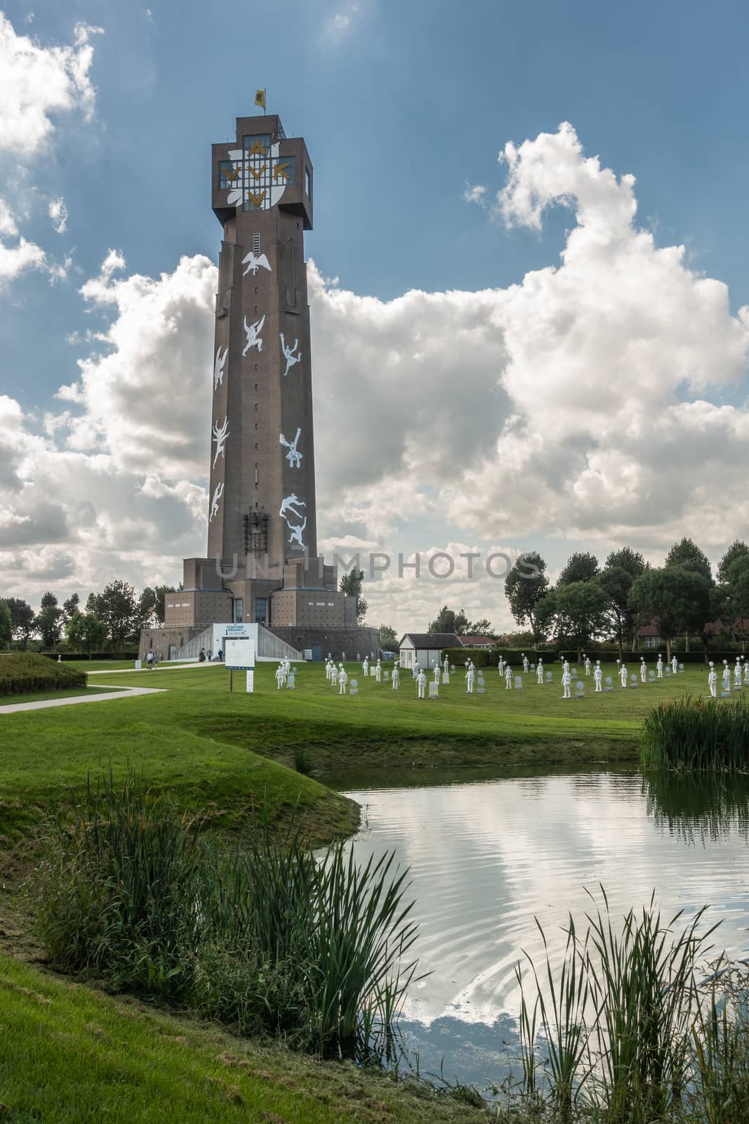 Diksmuide, Flanders, Belgium - September 15, 2018: Tallest peace monument in Flanders, called IJzertoren. brown bricks, white figures, blue sky with clouds, green lawn and reflecting pond.