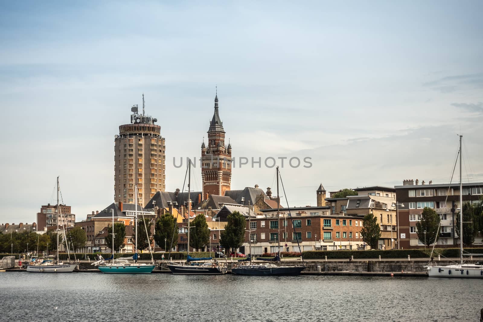 Dunkerque, France - September 16, 2018: Old Port with sailing yachts and two towers: condominiums, Belfry of Dunkirk town hall under light blue sky. Red brick other buildings.