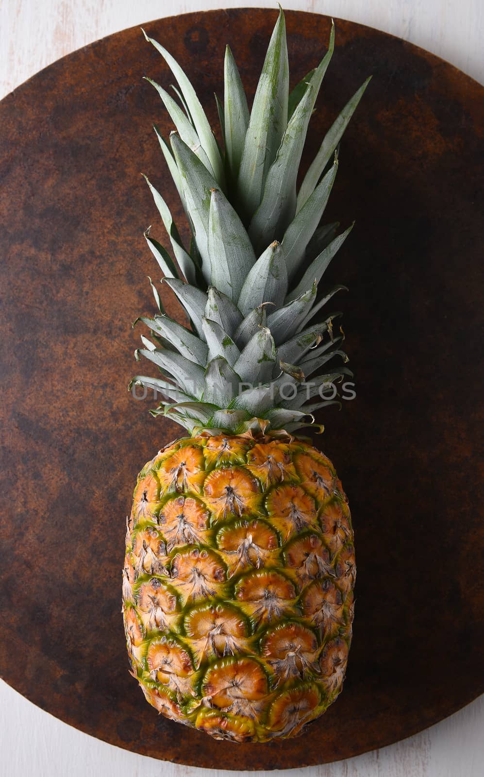 Top view of a fresh ripe pineapple on a round stone surface.