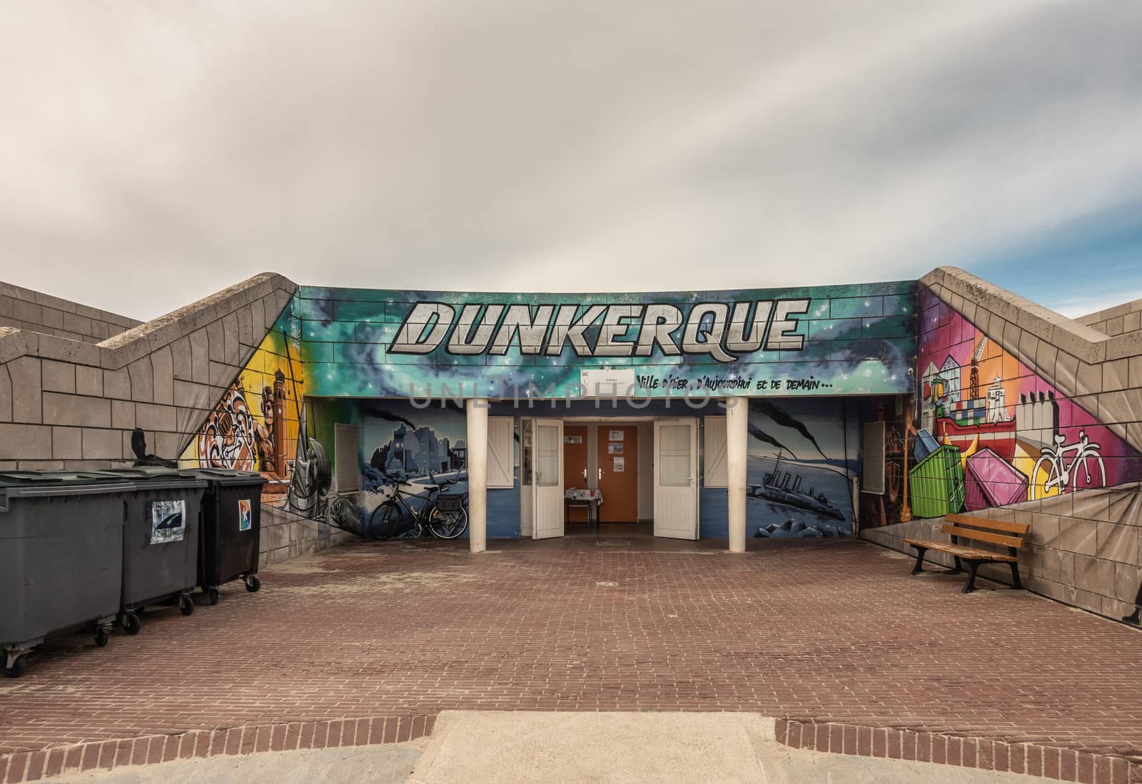 Dunkerque, France - September 16, 2018: Colorful wall paintings of Public toilet facilities on boardwalk along Dunkirk beach. Brown stone walls. White gray sky.