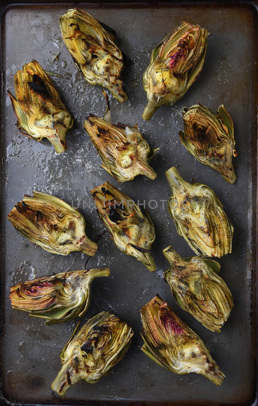 High angle view of grilled artichoke halves on a baking sheet.