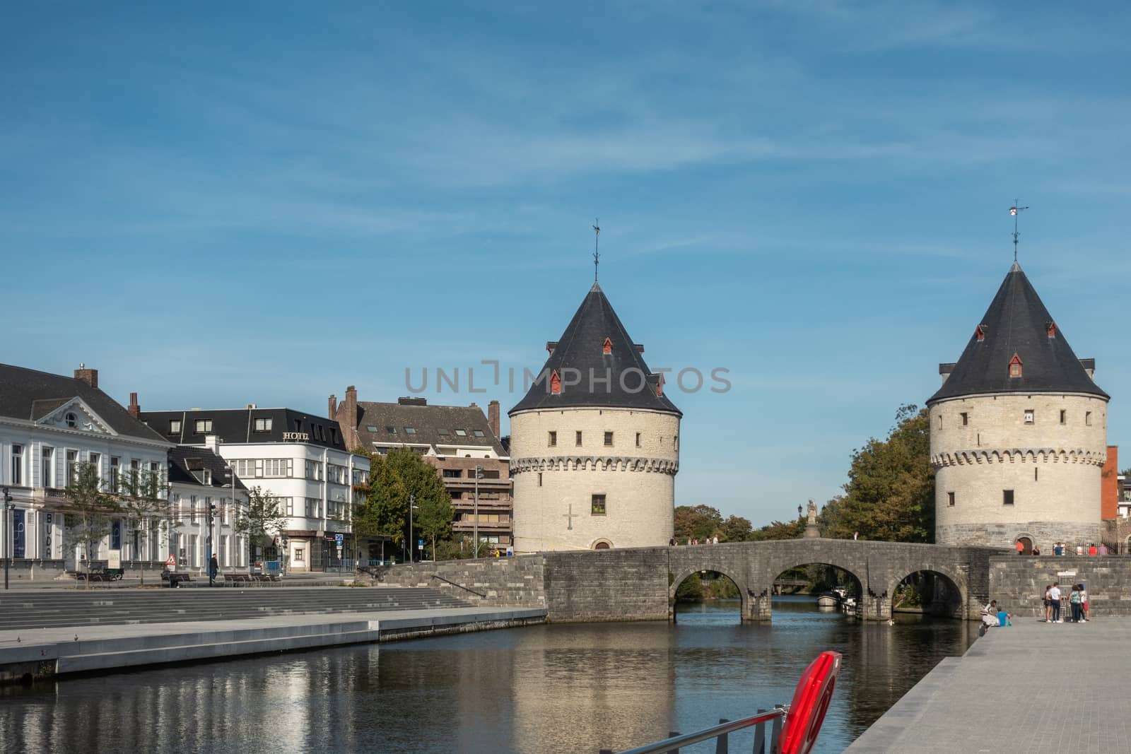 Kortrijk, Flanders, Belgium - September 17, 2018: Iconic pale brick Broel Towers on bridge over Lys River under blue sky. People and buildings on side.