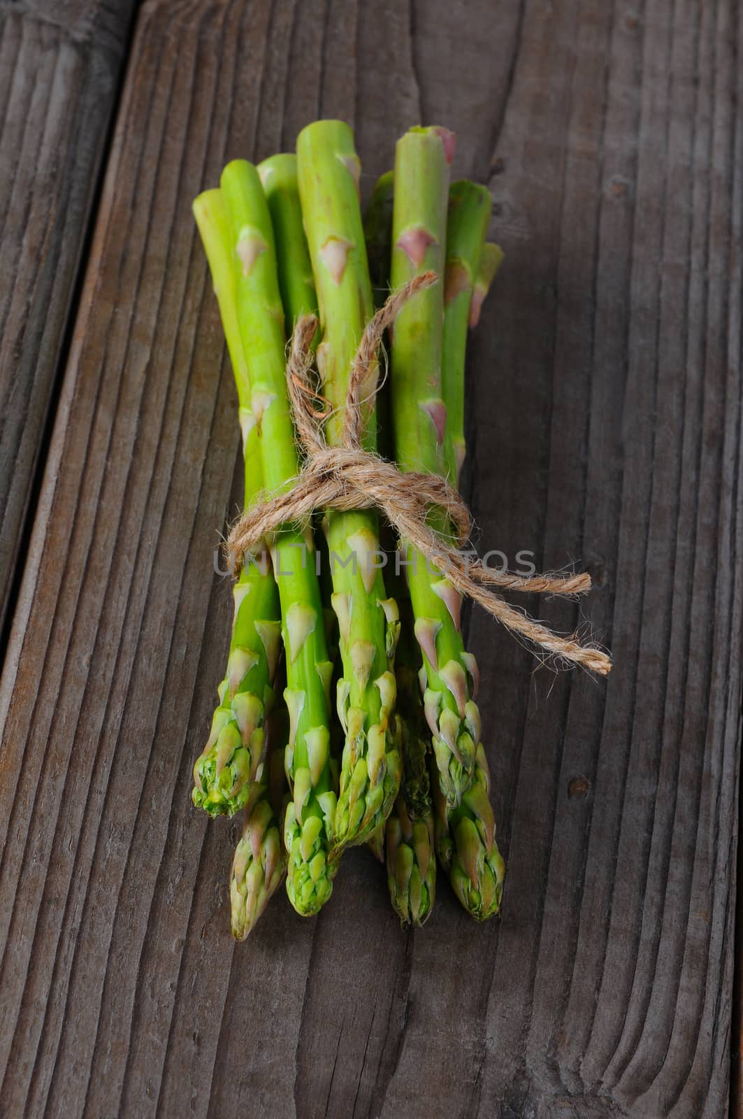 A bunch of asparagus tied with twine on a rustic wood background. Vertical format. 