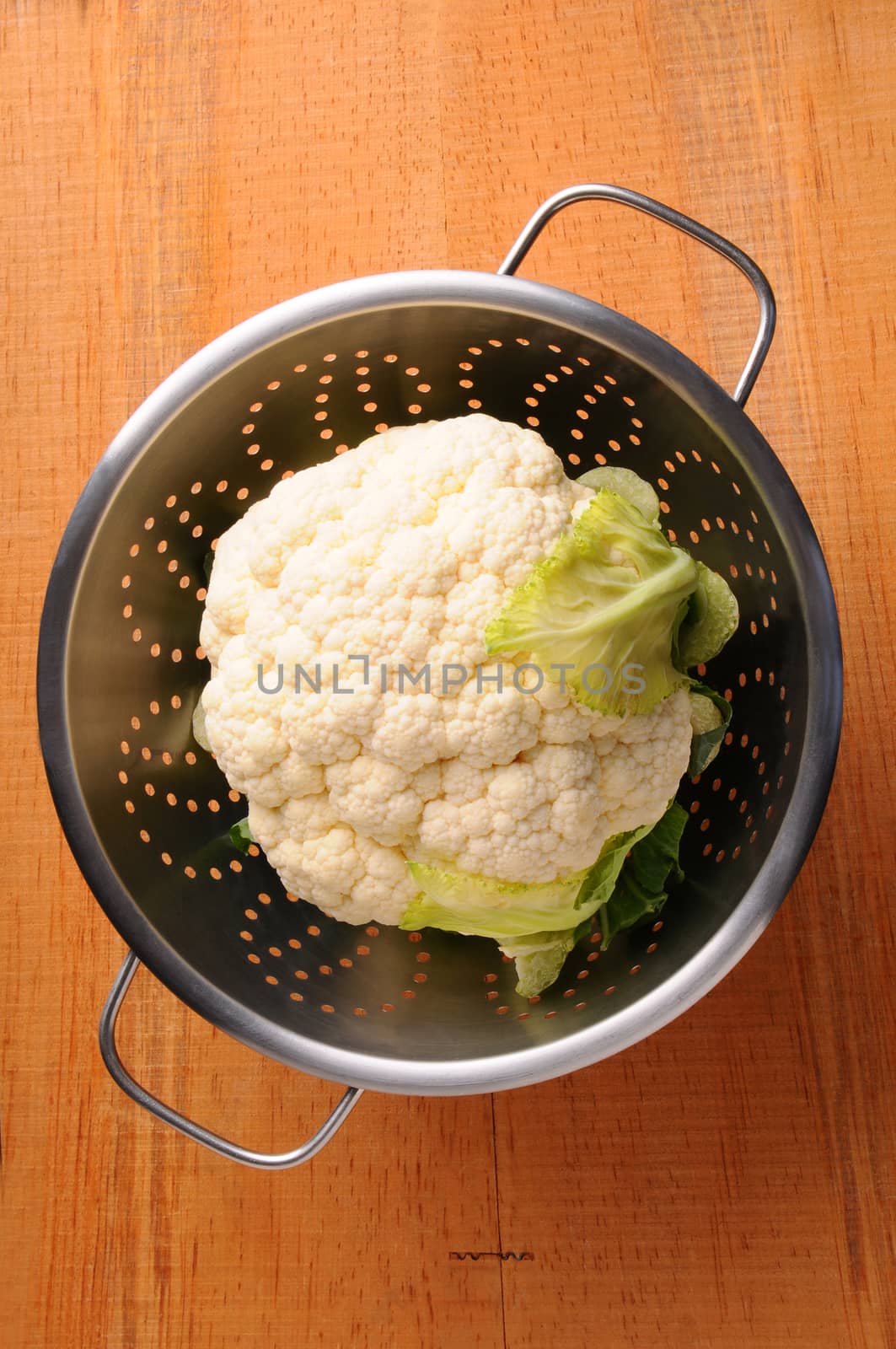 Fresh picked cauliflower in a metal colander on rustic wooden table. Vertical format shot from a high angle.