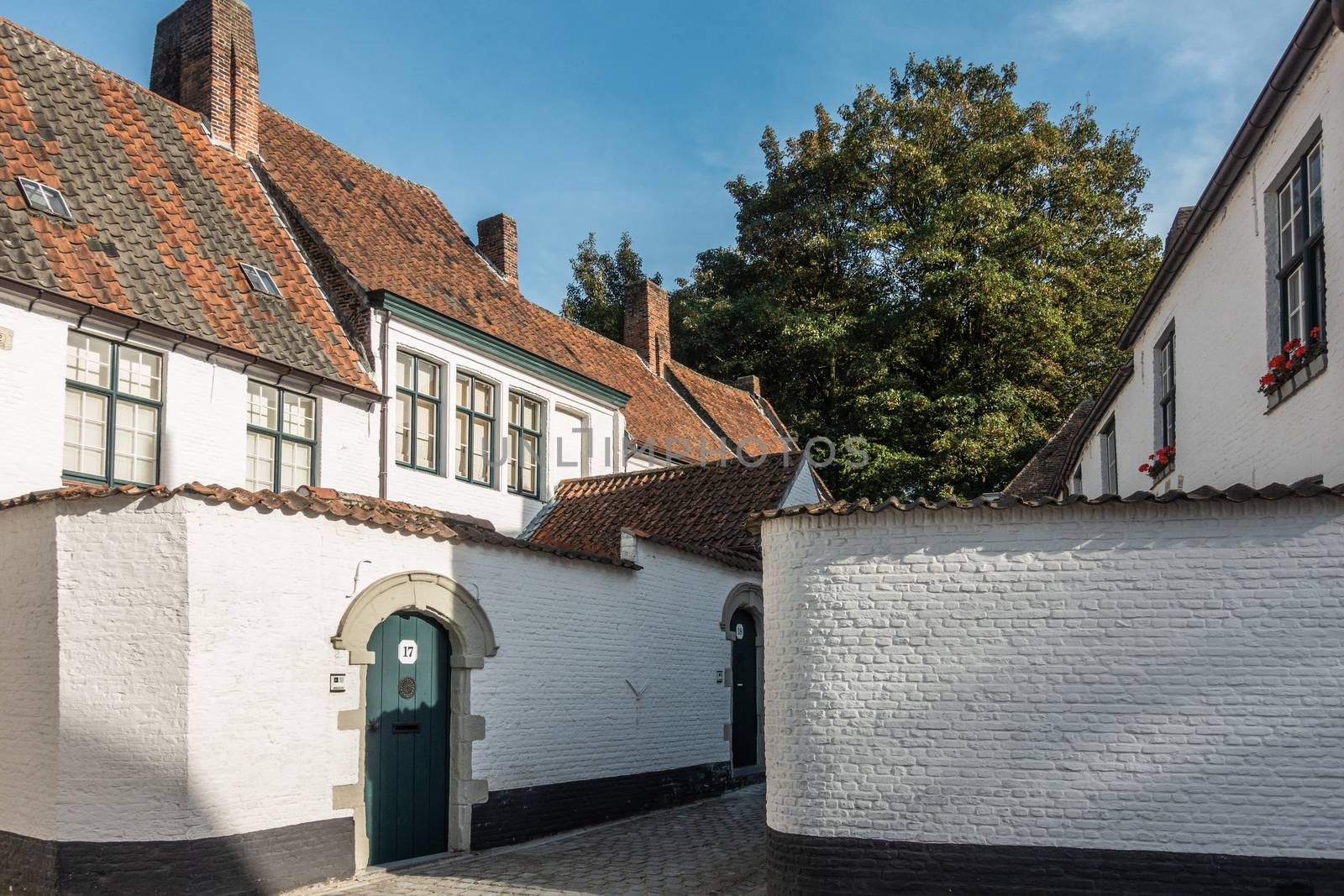 Kortrijk, Flanders, Belgium - September 17, 2018: Corner view of the beguinage with white and red roofed housing. Gray courtyard. Some green foliage.