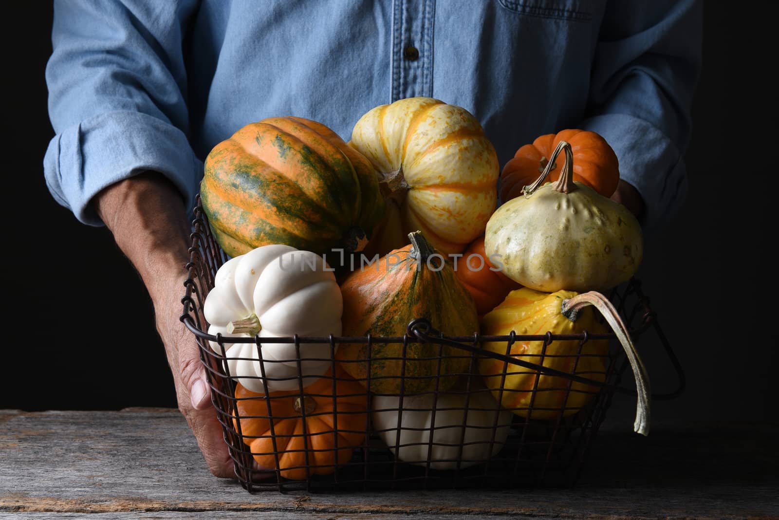 Farmer at his stand holding a wire basket of Autumn vegetables by sCukrov