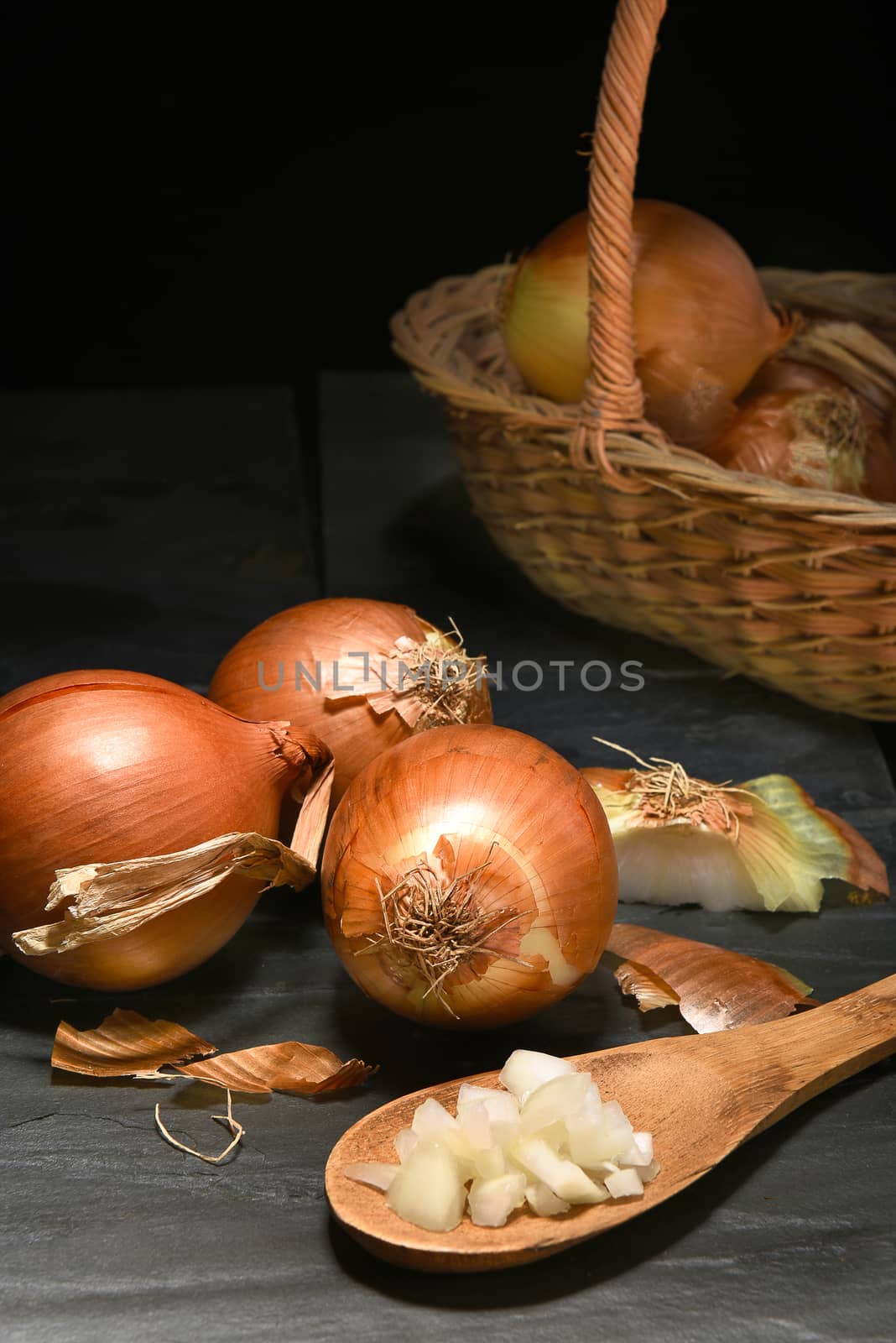 Closeup of a group of yellow onions on a dark slate surface. Vertical format with copy space.
