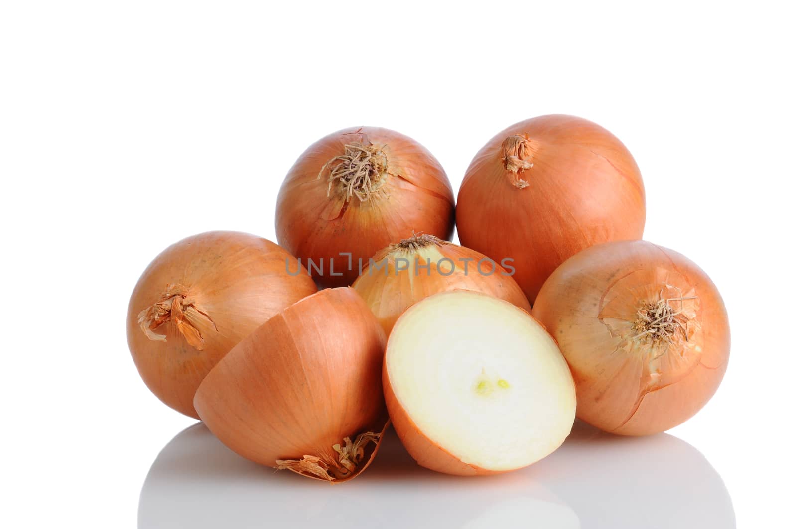 Closeup of a pile of yellow onions on a white surface with reflection. One onion is cut in half, horizontal format. 