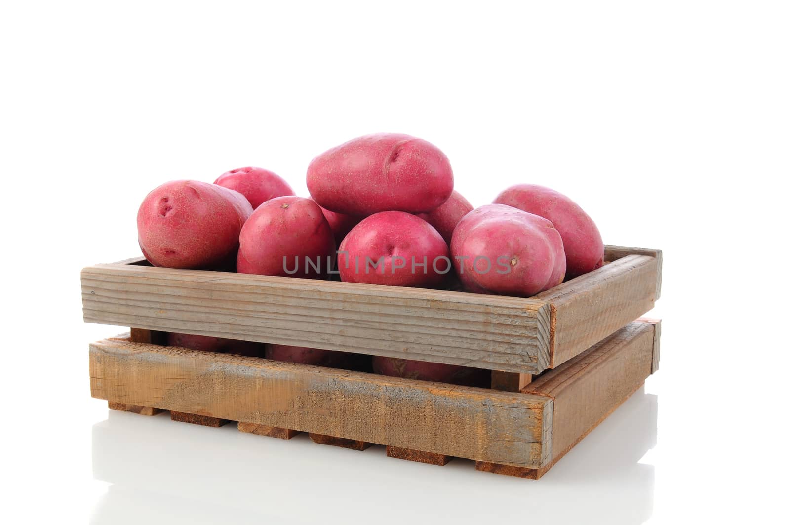 Red Potatoes in a wooden shipping crate. Horizontal format over a white background with reflection.