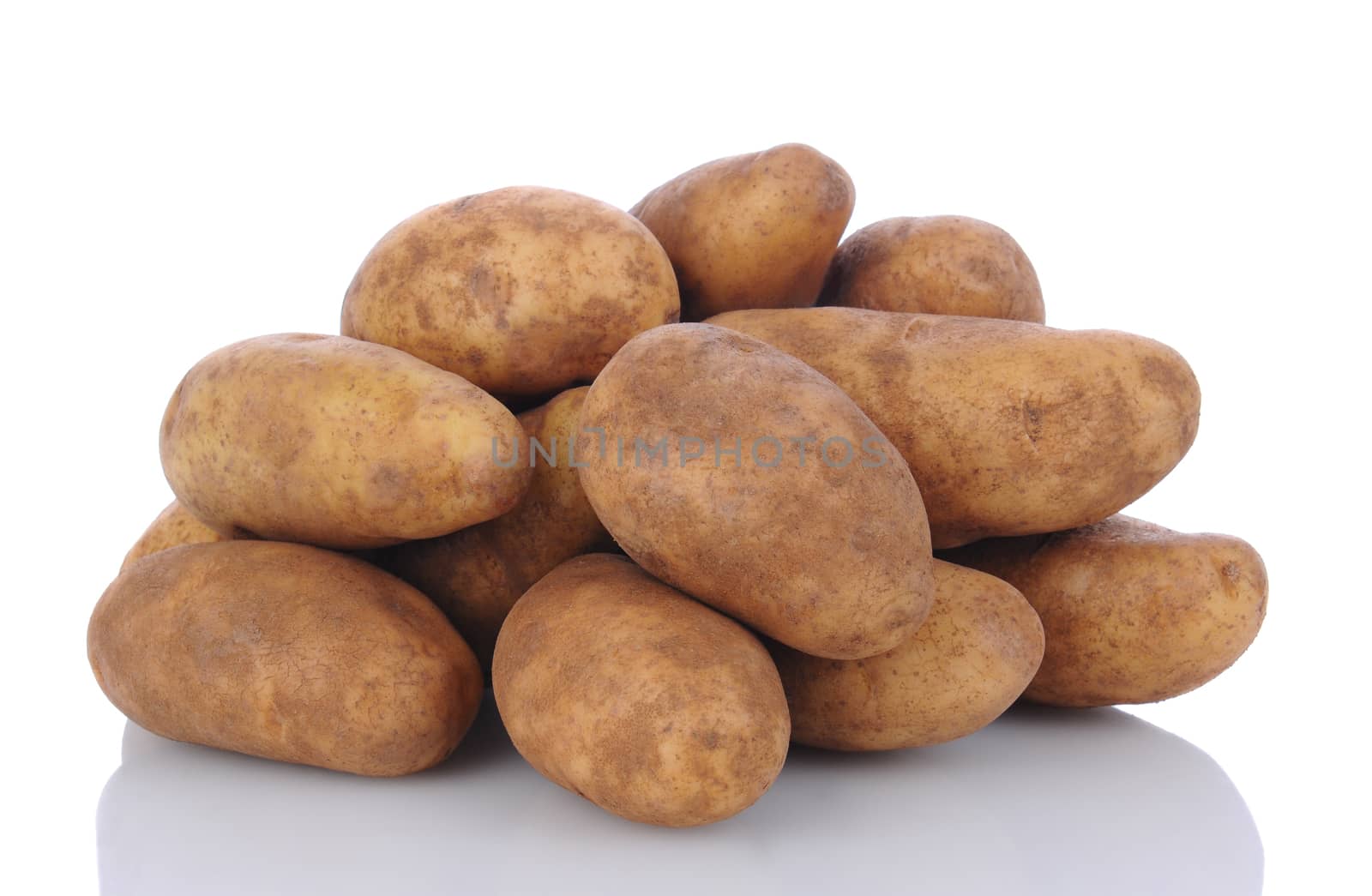 Closeup of a pile of russet potatoes on a white surface with reflection. Horizontal format.