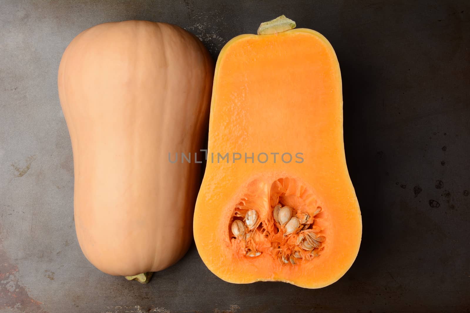 Butternut Squash on a metal cooking sheet. The fruit is cut in half showing both the inside and outside. Horizontal format. 