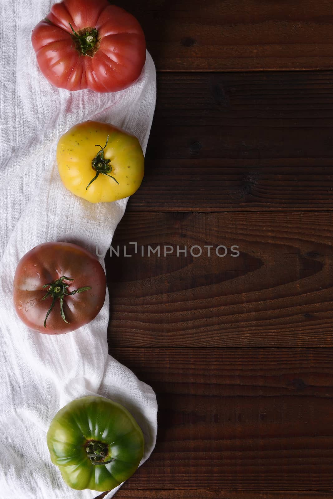 Top view of heirloom tomatoes on a kitchen towel and dark wood table.