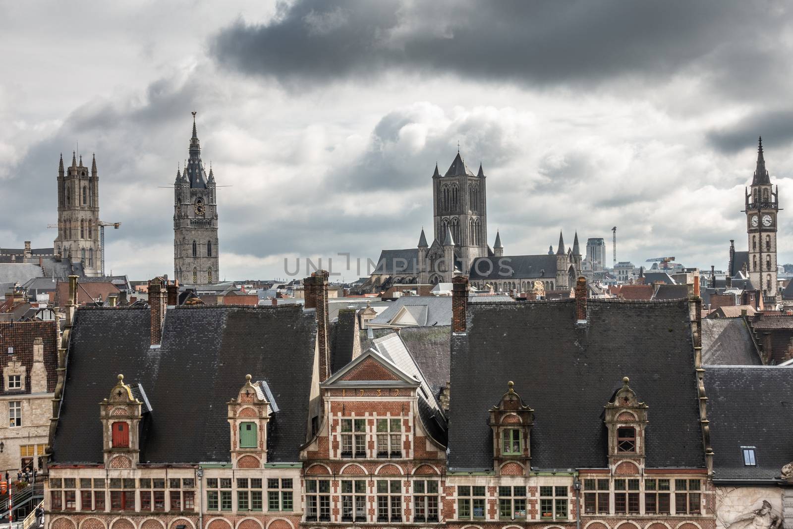 Ghent, Belgium - September 23, 2018: Seen from Gent Castle tower. Four towers LTR: Saint Bavo Cathedral, Belfry, Saint Nicolas church, Postal clock tower. Under heavy cloudscape of white on blue. Facades of Sint Veerleplein.