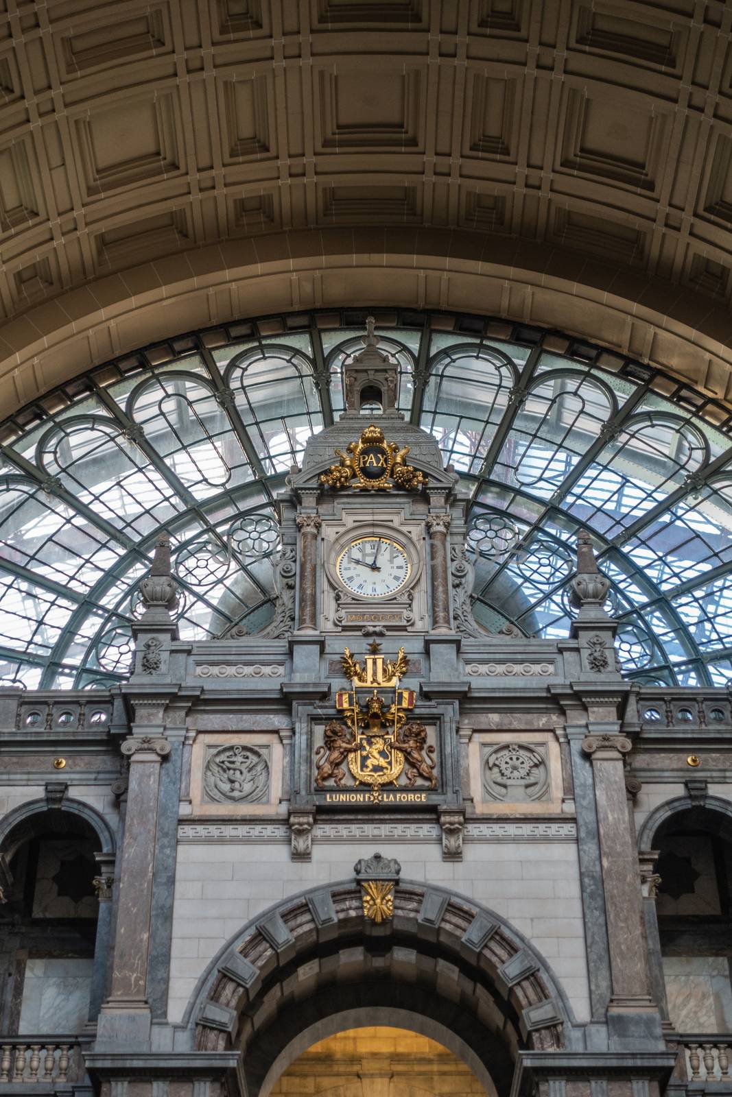 Antwerp, Belgium - September 24, 2018: Gray, beige, brown Monumental hall and arch over stairway to train hall at Antwerpen Centraal railway station. closeup of clock and Belgian coat of arms.