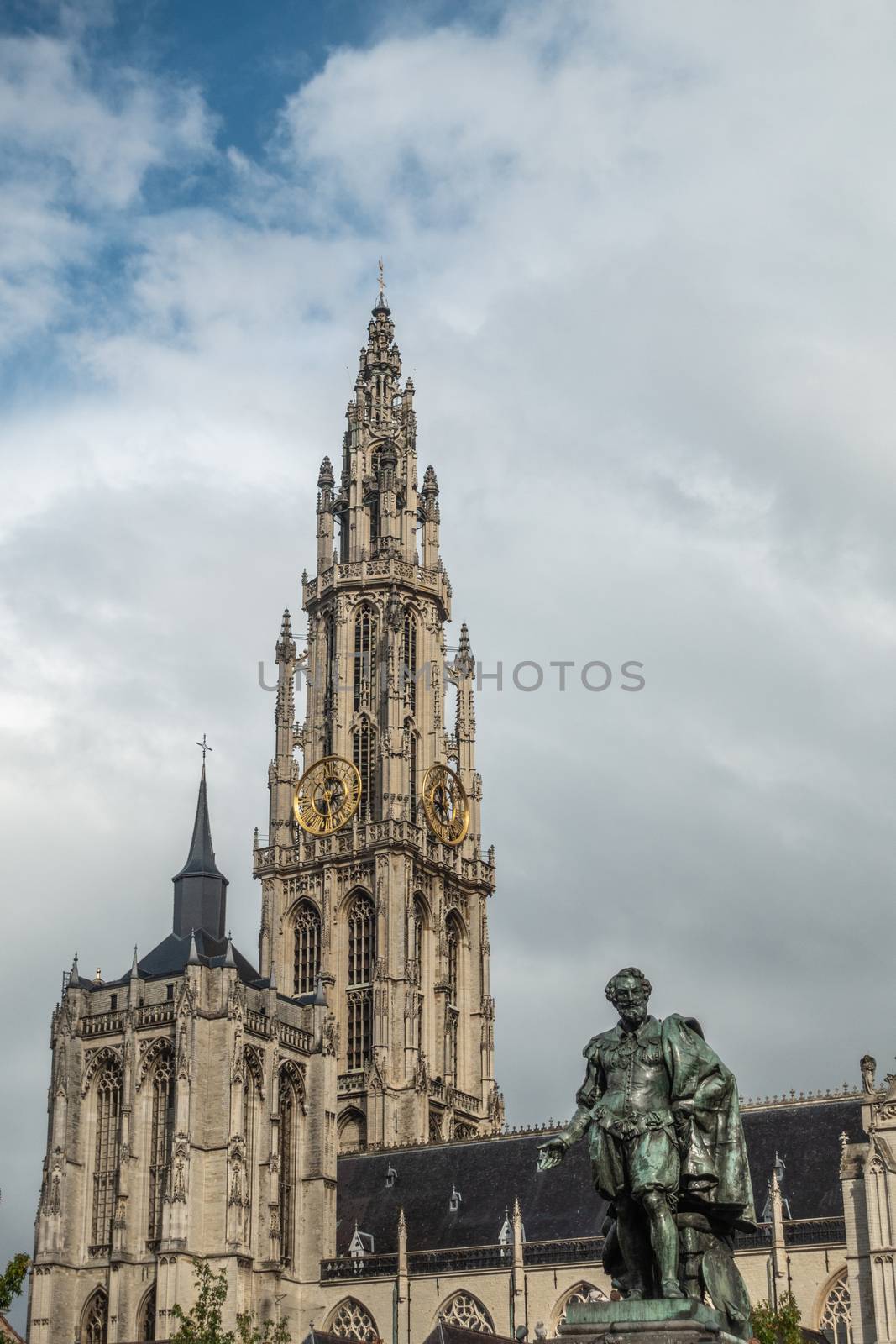 Antwerp, Belgium - September 24, 2018: Peter Paul Rubens bronze statue with towers of Onze-Lieve-Vrouwe Cathedral of Our Lady in back under white cloudy sky.