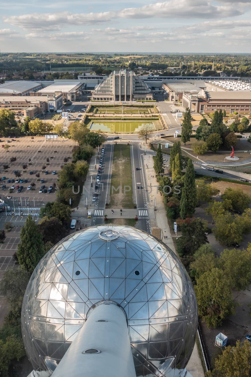 Brussels, Belgium - September 25, 2018: The historic world expo halls shot from top of the Atomium monument. Green belt and cloudy sky on horizon. One of the Atomium spheres up front.
