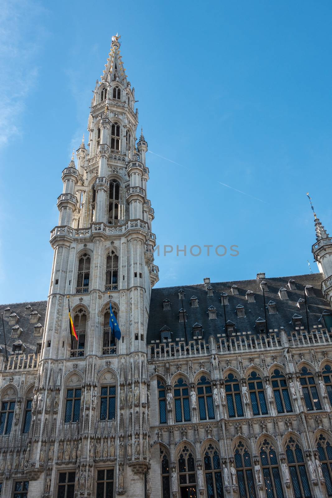 Brussels, Belgium - September 26, 2018: Spire and facade of gray stone town hall with statues and against blue sky.