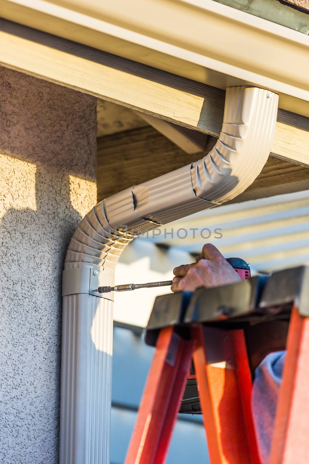 Worker Attaching Aluminum Rain Gutter and Down Spout to Fascia of House.