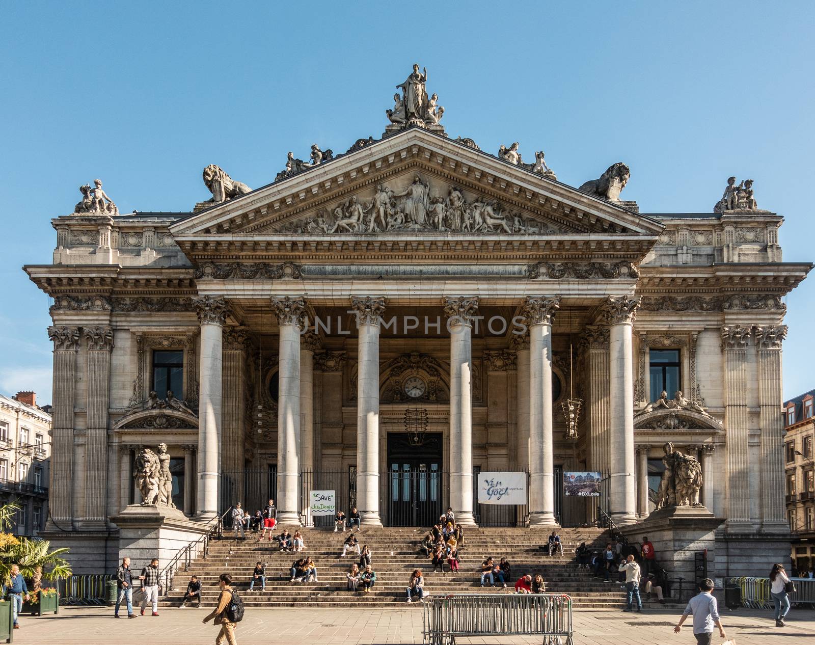 Brussels, Belgium - September 26, 2018: Brown stone Stock Exchange building as Greek temple with pillars, statues and frescoes. People on stair. Blue sky.