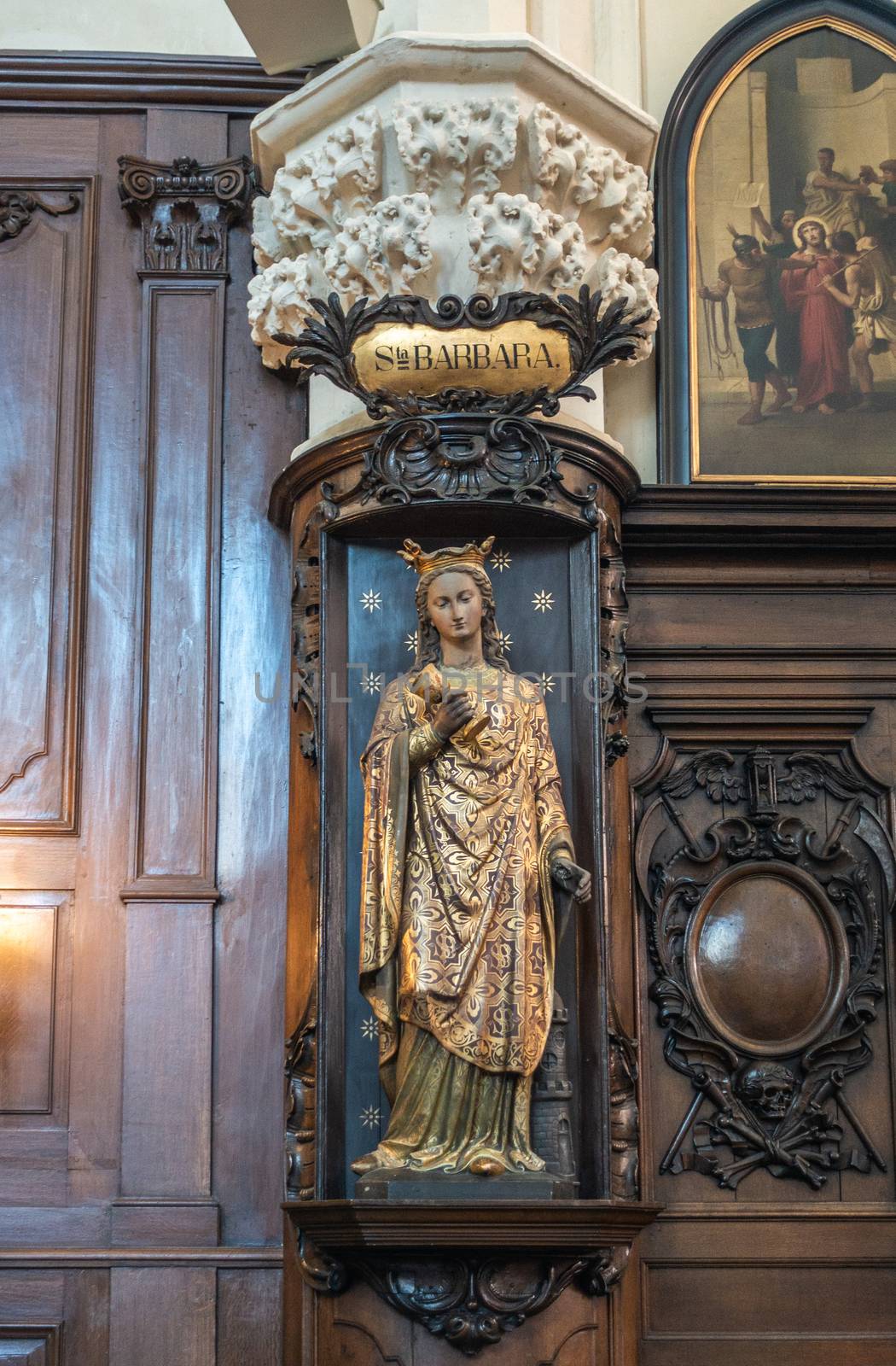Brussels, Belgium - September 26, 2018: Inside Saint Nicolas Church. Santa Barbara statue with golden dress against dark wooden sculpted panels. Paining of arrest of Jesus.