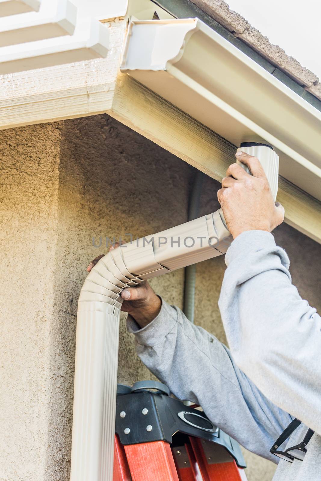 Worker Attaching Aluminum Rain Gutter and Down Spout to Fascia of House. by Feverpitched