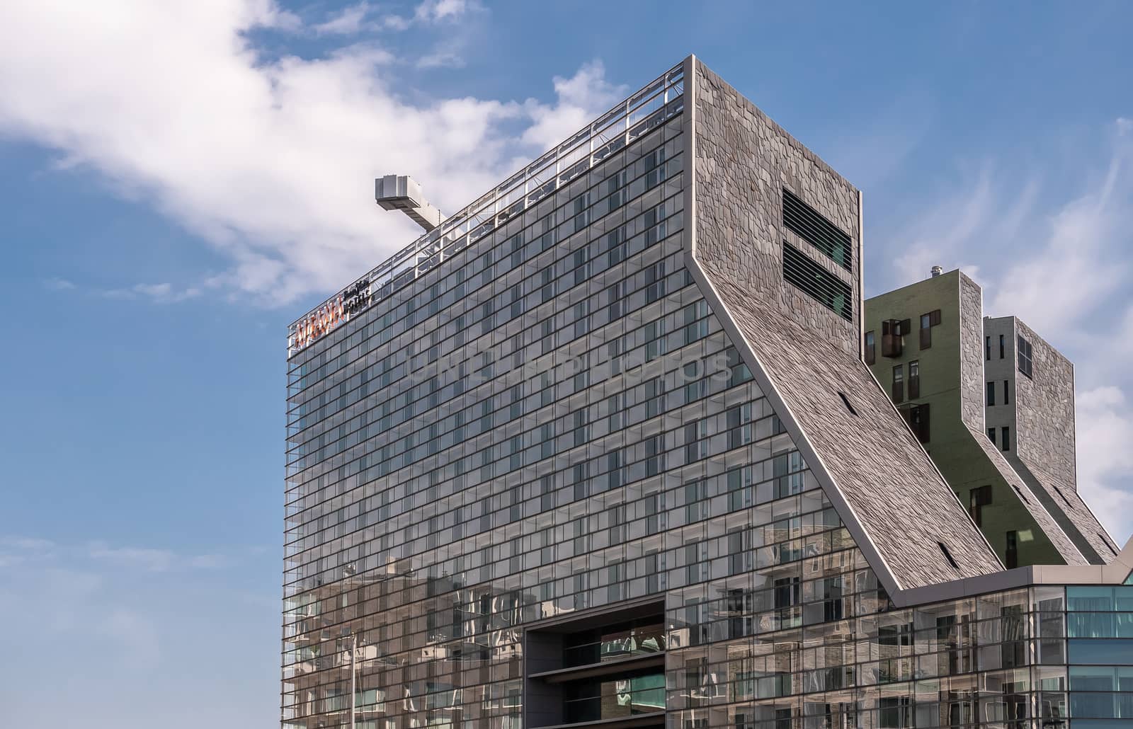 Amsterdam, the Netherlands - June 30, 2019: Modern architecture Building with gray glass wall of Mate Aitana Hotel on IJdok under blue sky with white clouds.
