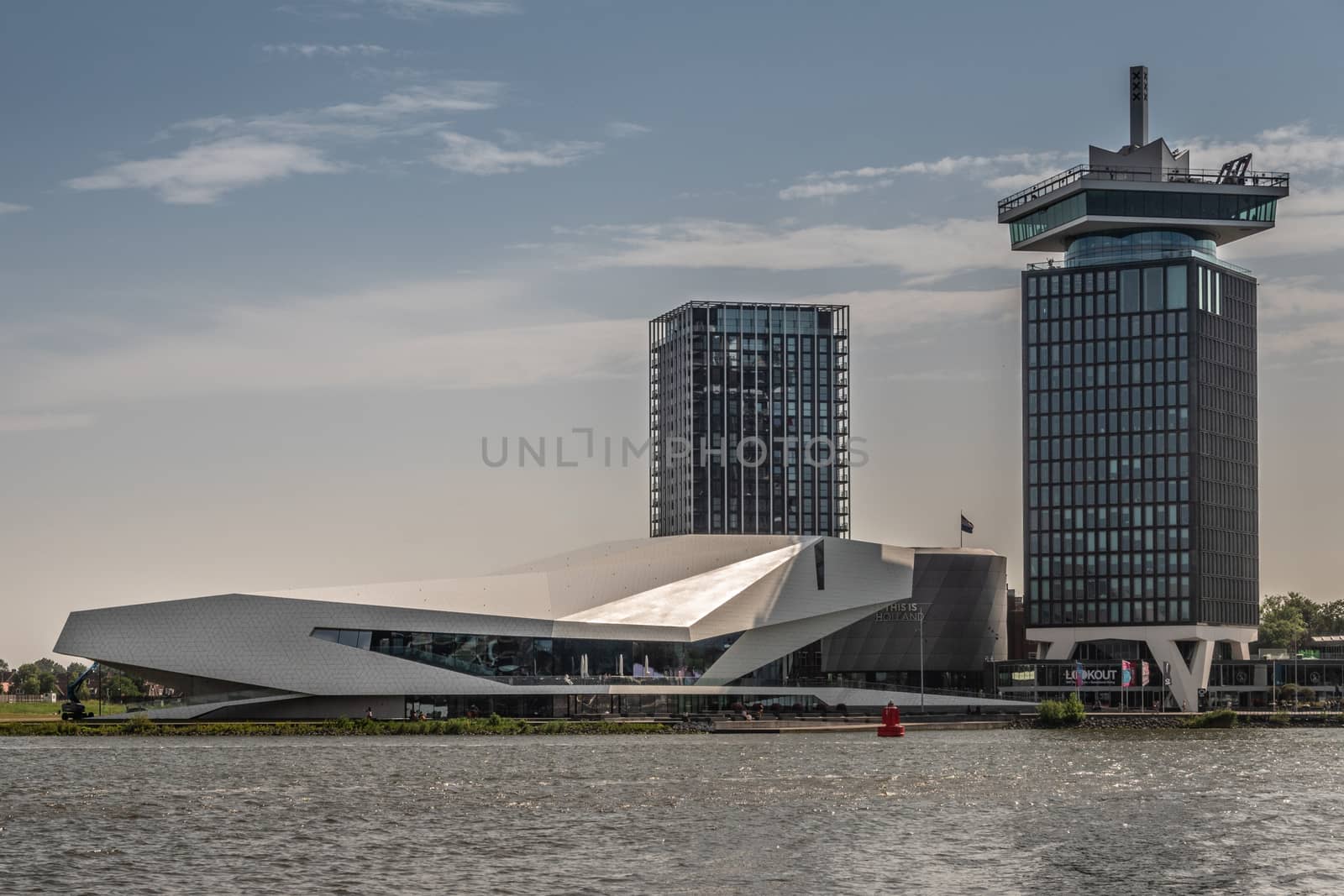 Amsterdam, the Netherlands - June 30, 2019: White Eye Film Museum, A’Dam lookout tower to the right, Clinknoord tower to the left under morning lighted sky. IJ water in front.
