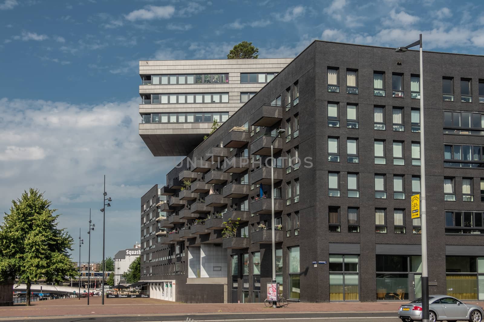 Amsterdam, the Netherlands - June 30, 2019: Modern architecture office building on Westerdokplein has section with dark walls and other part on top with white gray walls. Blue sky, green foliage.