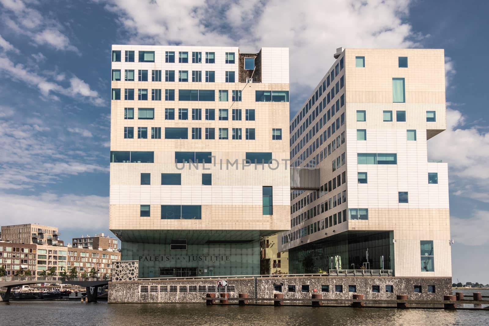 Amsterdam, the Netherlands - June 30, 2019: Cubic modern architecture of white large Justice Palace on IJdok under blue sky with white clouds. Name of the occupant is spelled out in Dutch above entrance.
