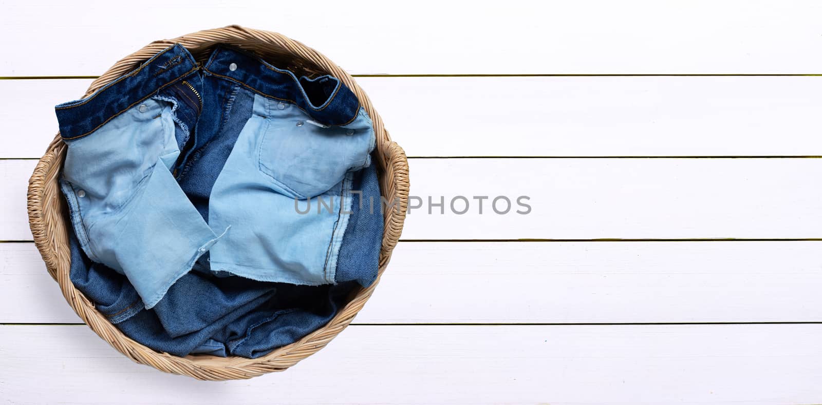 Jeans in laundry basket on white wooden background. Copy space