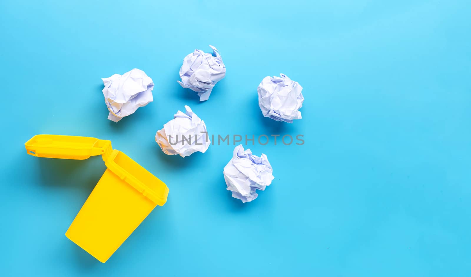 Yellow bin with white crumpled paper on blue background. Top view