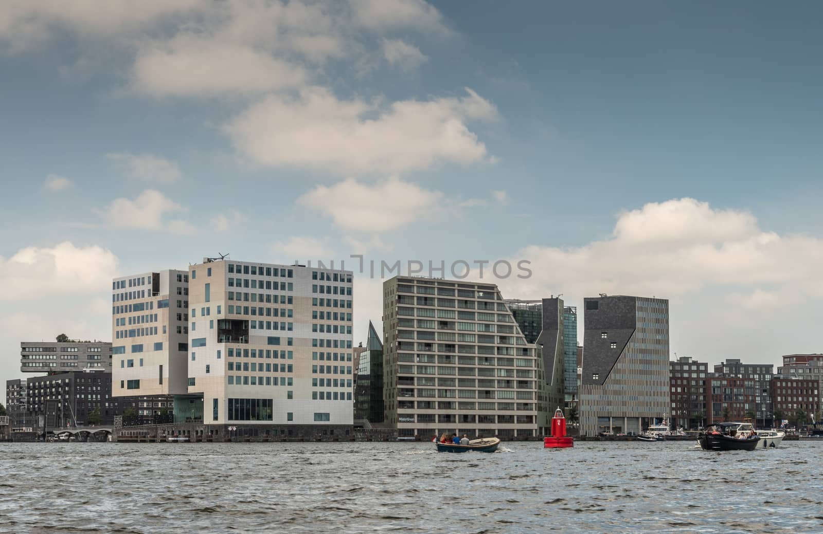 Amsterdam, the Netherlands - June 30, 2019: Cubic modern architecture of white large Justice Palace on IJdok under blue sky with white clouds. Other office buildings. Pedestrian bridge and IJ water.