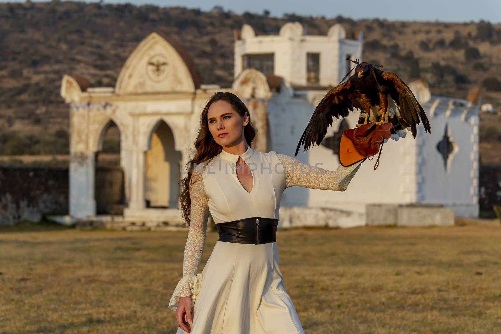 A gorgeous Hispanic Brunette model poses outdoors with a falcon outdoors at a hacienda