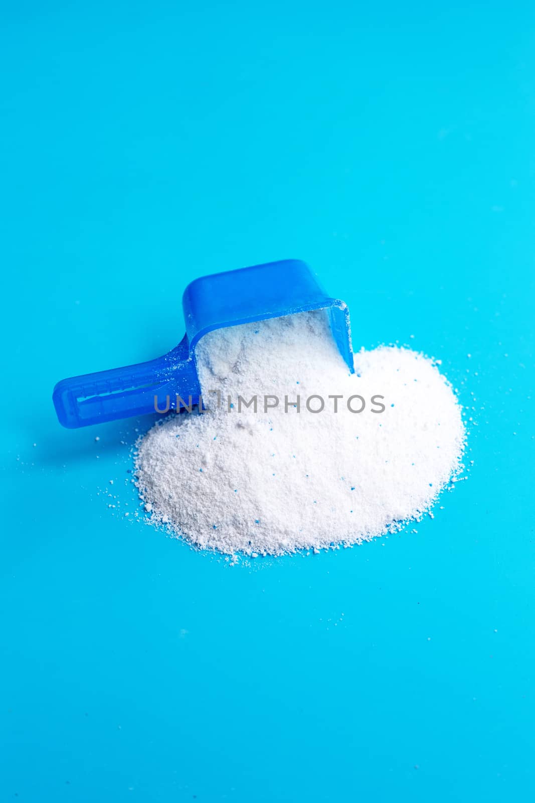 Detergent powder with measuring spoon  for clothes washing on blue backgrond. Laundry concept.