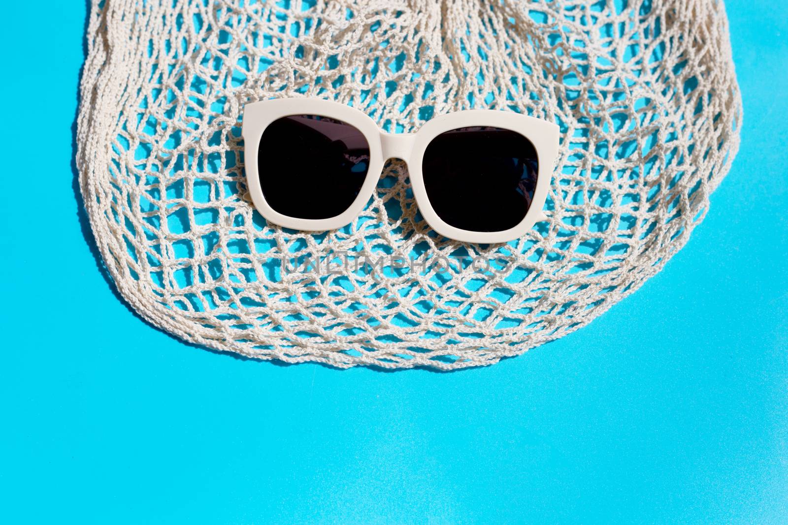 Sunglasses with mesh bag on blue background. Enjoy holiday concept. Copy space
