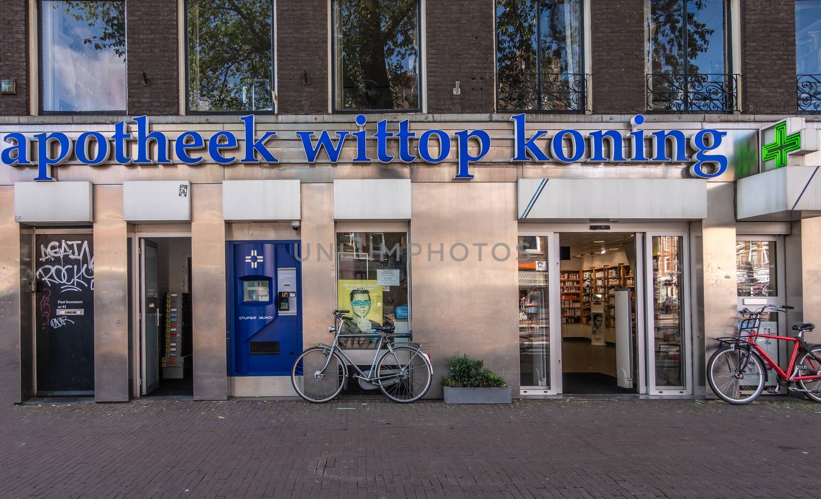 Amsterdam, the Netherlands - July 1, 2019: Facade of pharmacy Wittop Koning with bikes in front, dark blue name sign and the classic green cross light. Located in street called Overtoom.