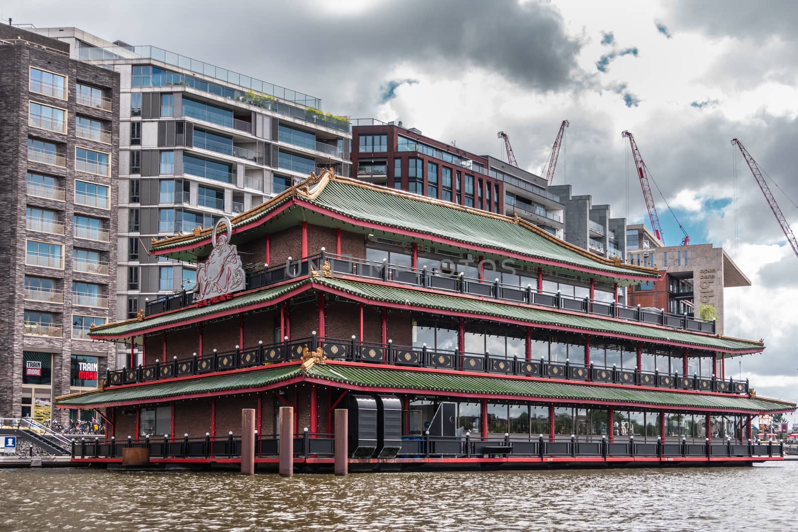 Amsterdam, the Netherlands - July 1, 2019: Red-green-brown long facade with huge white Buddha statue of Sea Palace floating restaurant at Oosterdokskade under heavy cloudscape.