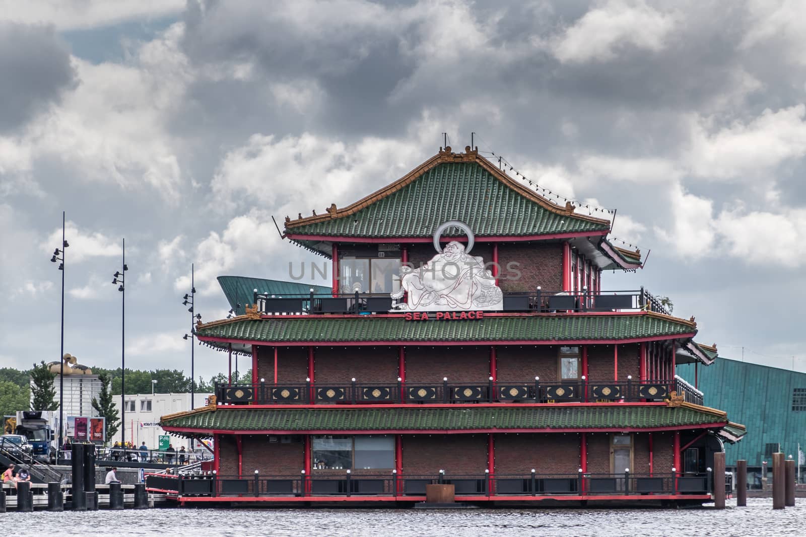 Amsterdam, the Netherlands - July 1, 2019: Red-green-brown short facade with huge white Buddha statue of Sea Palace floating restaurant at Oosterdokskade under heavy cloudscape.