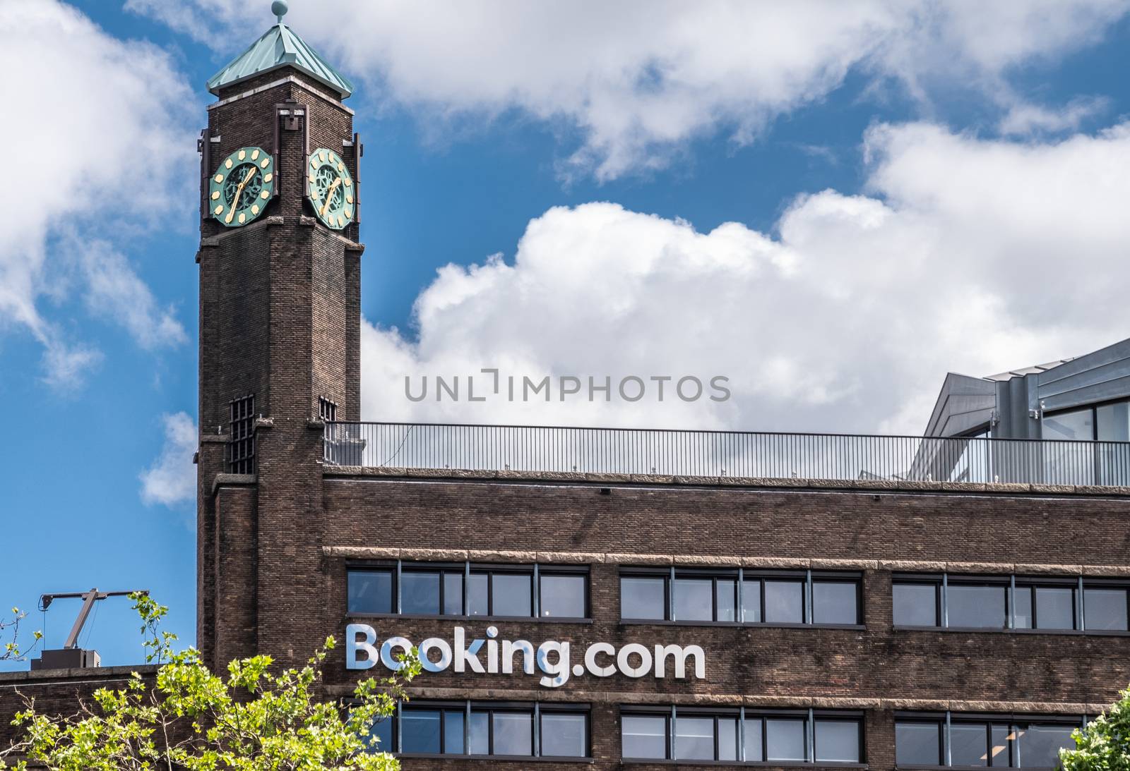 Amsterdam, the Netherlands - July 1, 2019: Rembrandtplein. De dark brown brick office building with clock tower of booking.com against blue sky and white clouds.