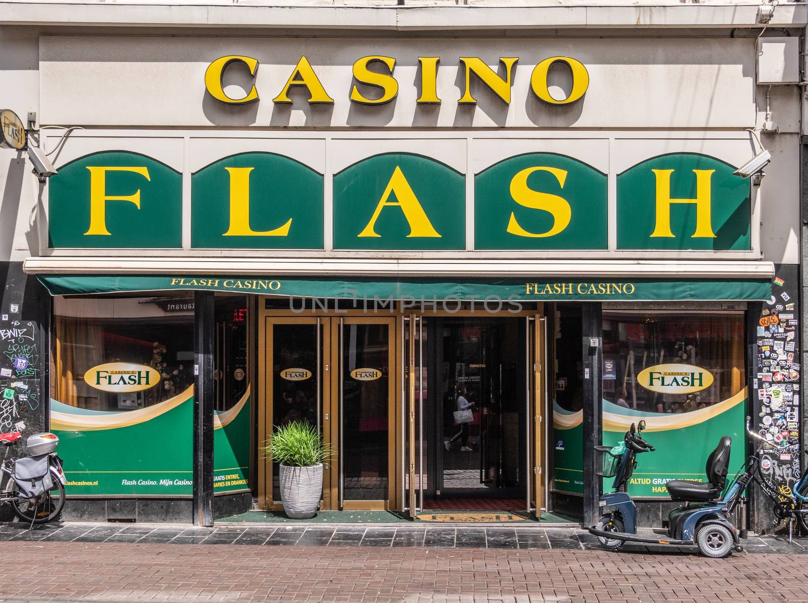 Amsterdam, the Netherlands - July 1, 2019: Green-white entrance and display window of Flash Casino with motorized wheelchair up front.