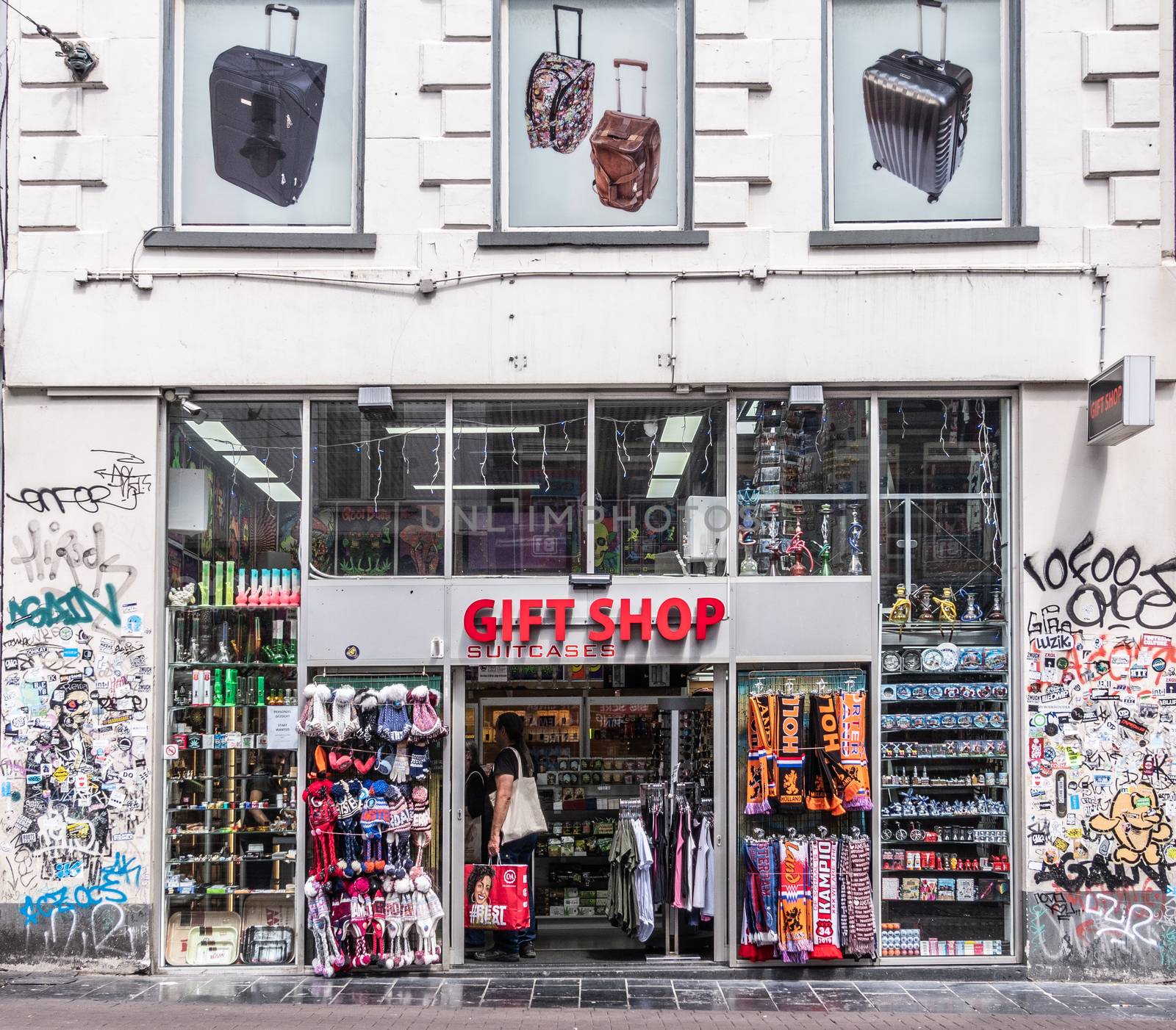Amsterdam, the Netherlands - July 1, 2019: Gift shop entrance and facade with items on display set in white wall, covered in graffiti and stickers.