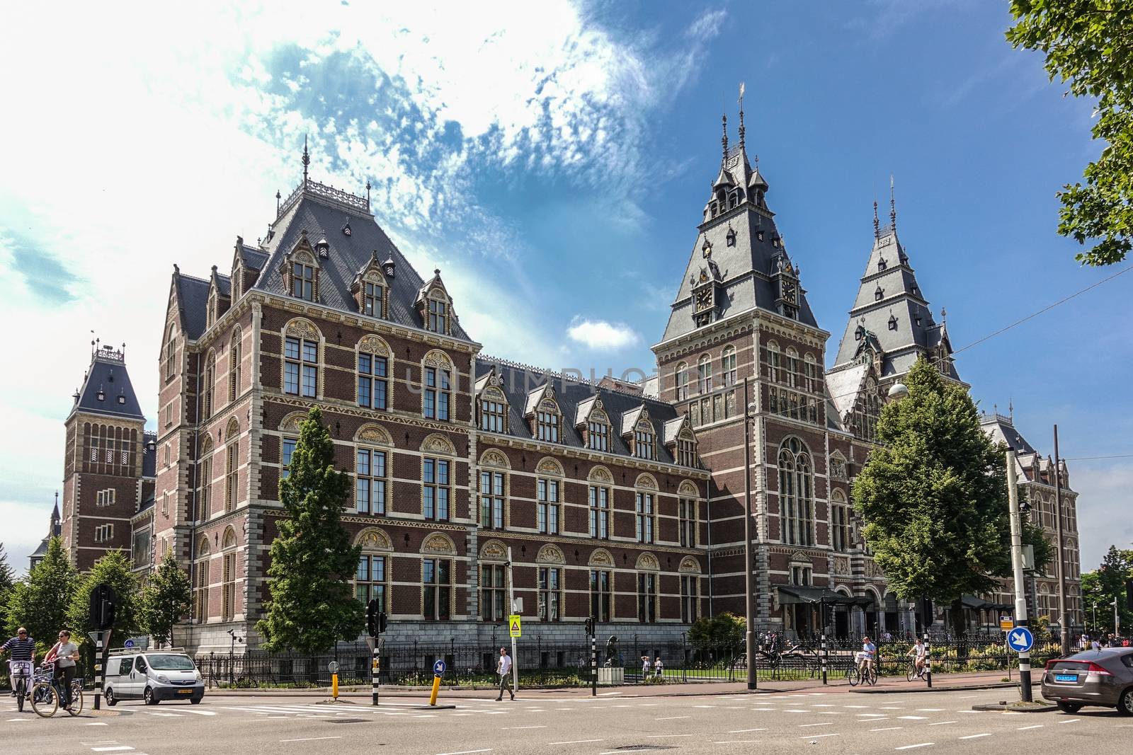 Amsterdam, the Netherlands - June 30, 2019: Wide shot of Rijksmuseum Monumental facade with towers in beige and red bricks. Under blue-whtie cloudscape. People in front.