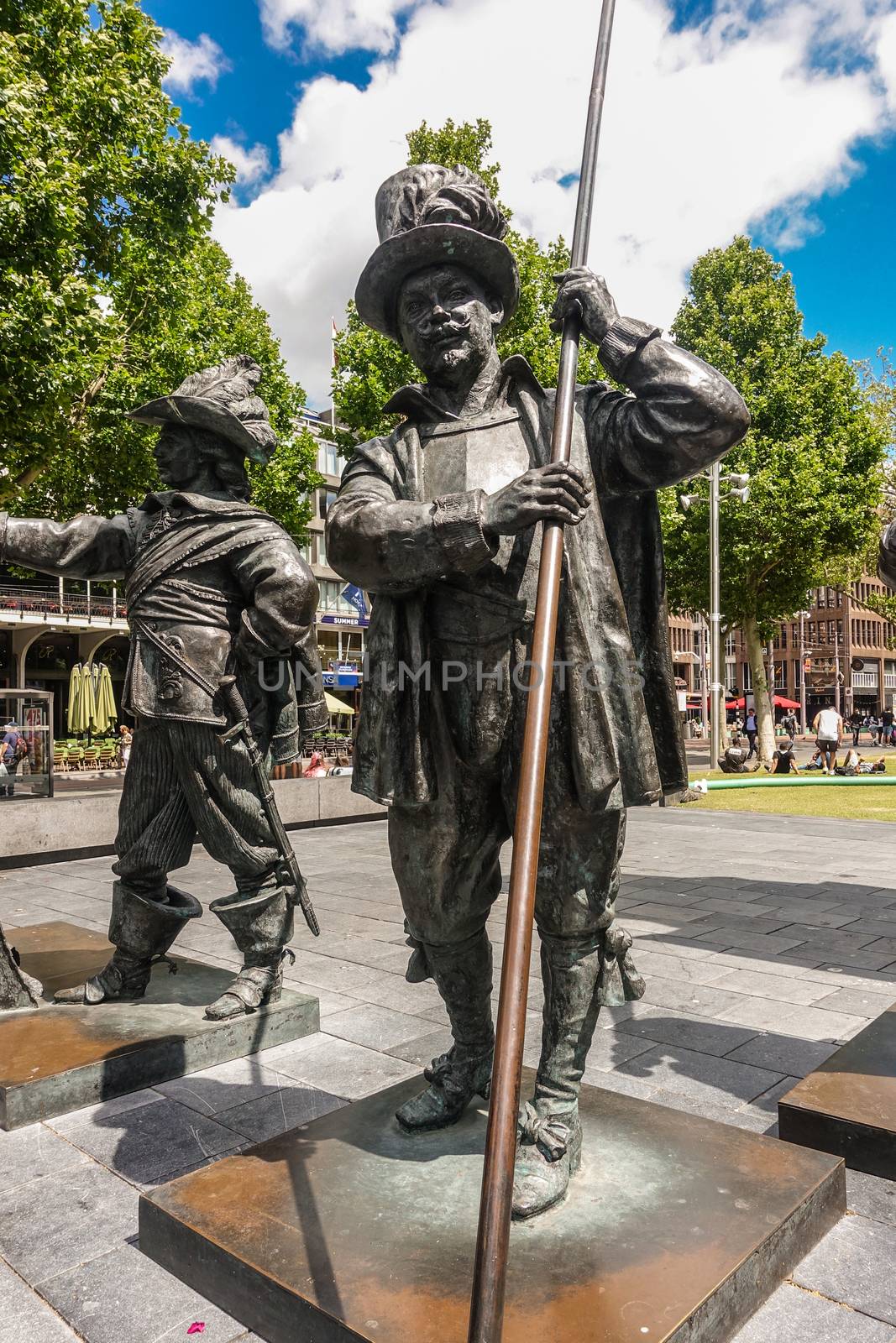 Amsterdam, the Netherlands - July 1, 2019: De Nachtwacht compostion of statues on Rembrandtplein. Closeup of full body of one of several figures against green foliage and buildings. Holds lance.